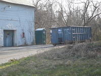 Tere are a few buildings with dumpsters outside them.   Each of these dumpsters is full.
